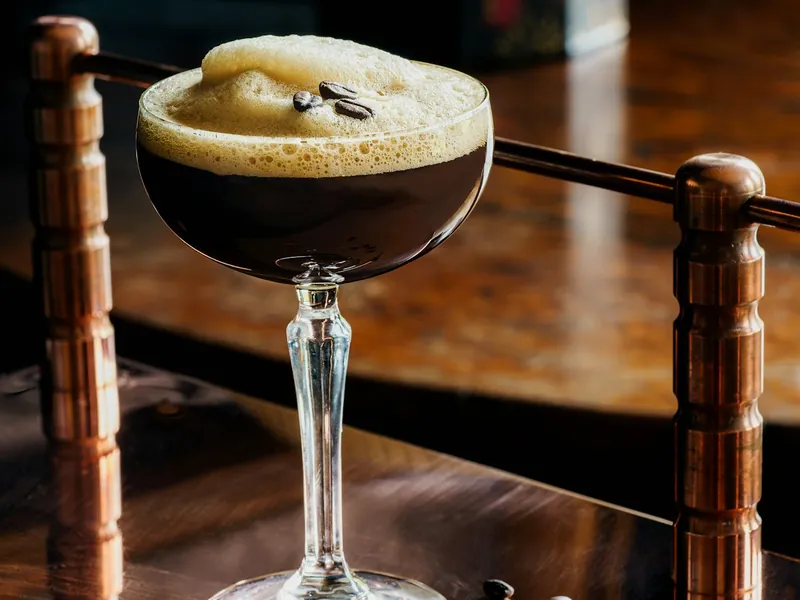 Espresso martini with a foam top in a coupe, coffee beans beside it