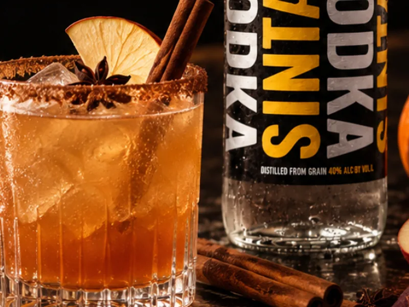 Spiced apple cocktail with a cinnamon-sugar rim, apple slice and cinnamon stick, next to a bottle of SINTAX Vodka